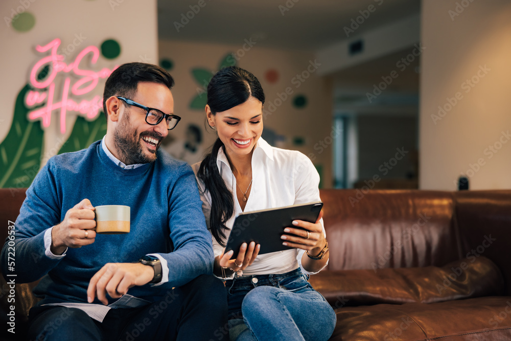 Smiling female and male employees surfing the web over the digital tablet, sitting at the office.