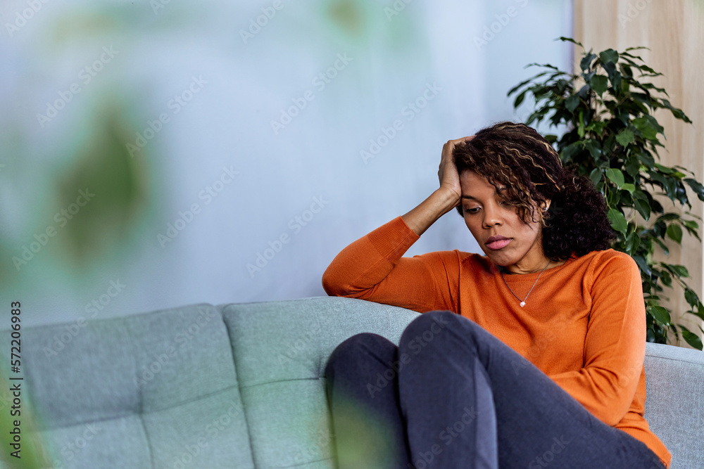 A depressed African woman looking down and touching her forehead.