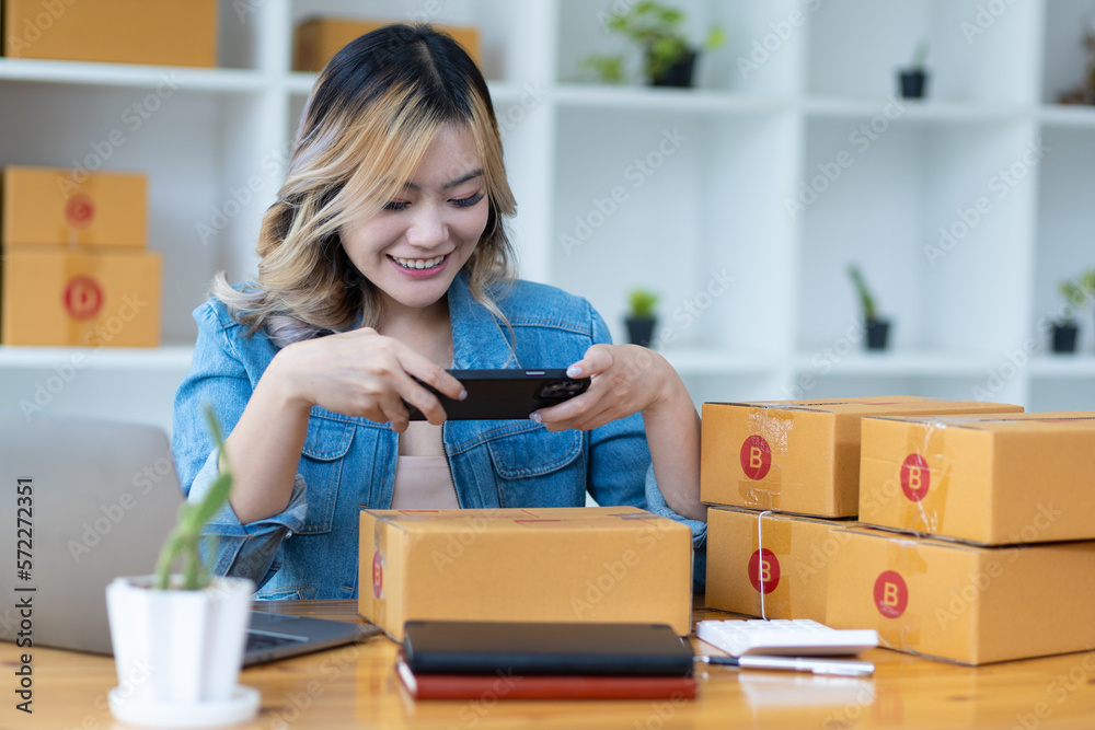 Female small business owner using mobile app on smartphone scanning barcode checking parcel box. Wom