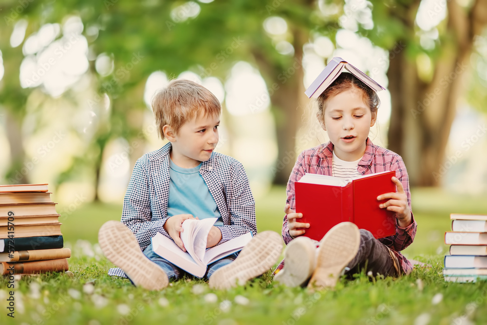 Boy and girl sitting on the meadow with books in their hands.