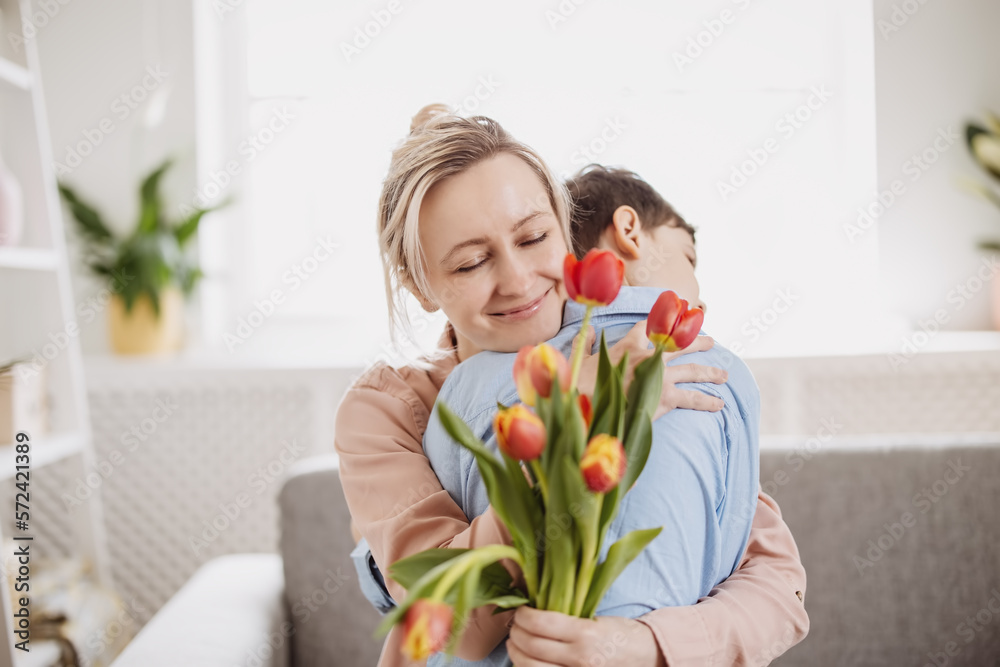 Cute boy sitting on the sofa with mom and giving a bouquet of tulips to her.