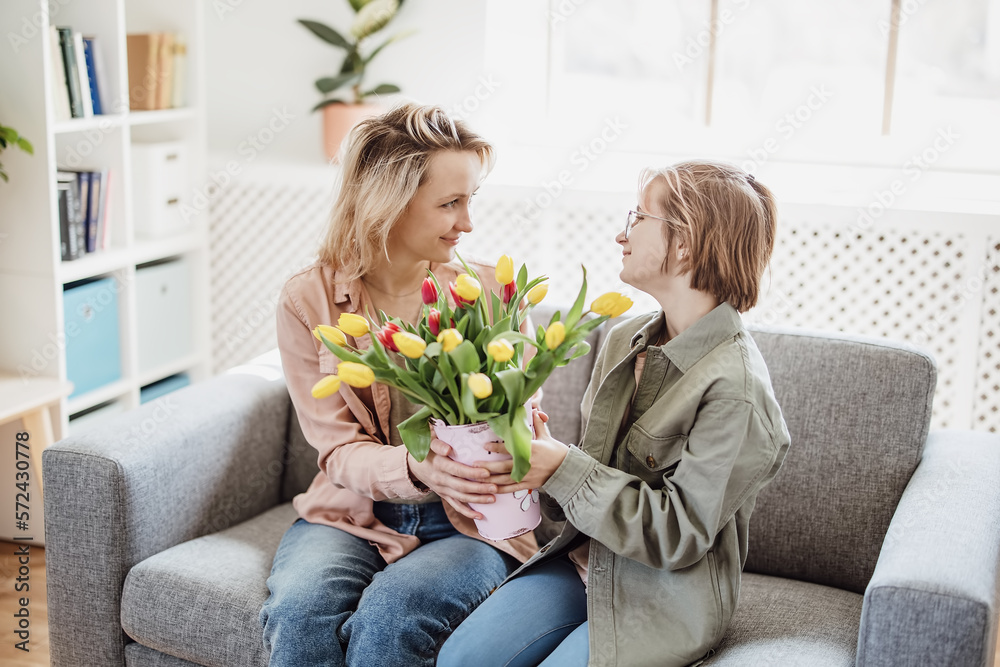 Mother and daughter sitting on the sofa with tulips in their hands indoor.