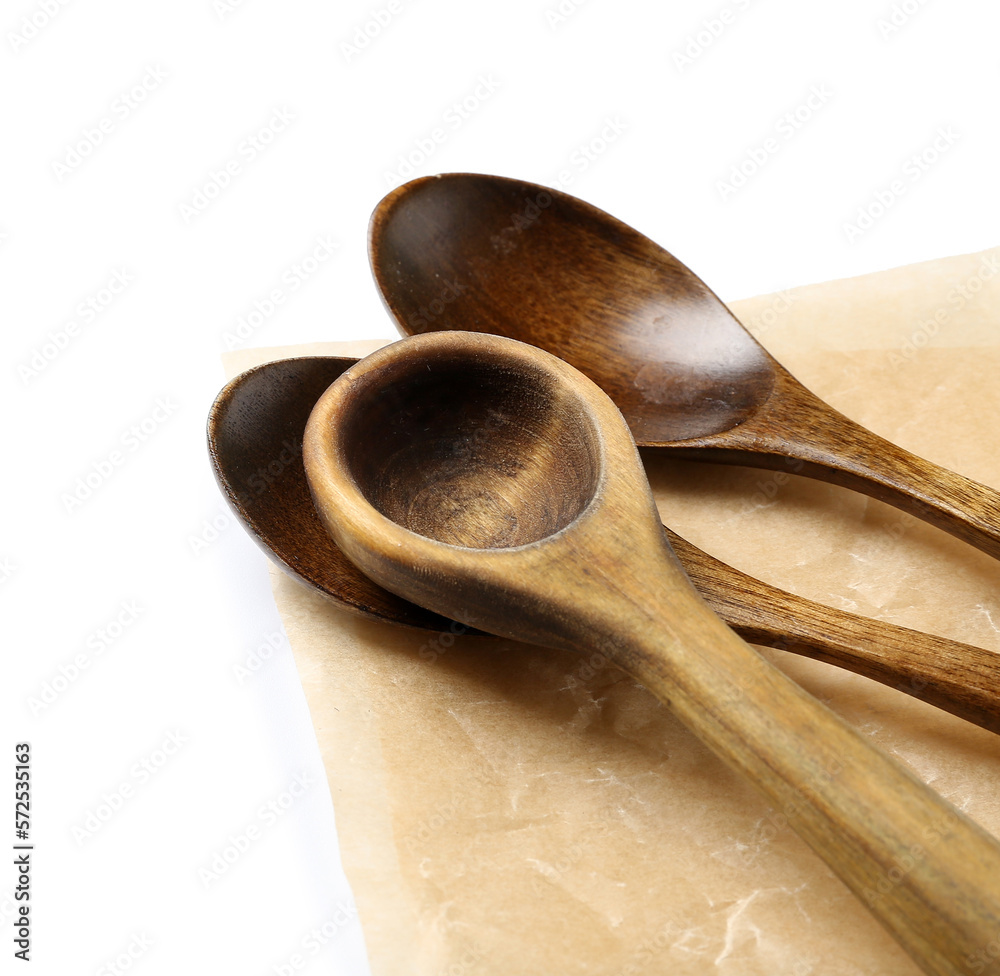 Wooden spoons and sheet of baking paper on white background, closeup