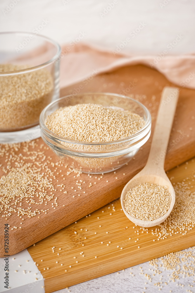 Wooden boards with bowl and spoon on amaranth seeds on table, closeup