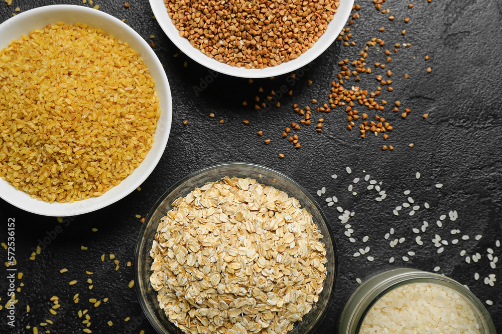 Bowls of different cereals on dark background, closeup