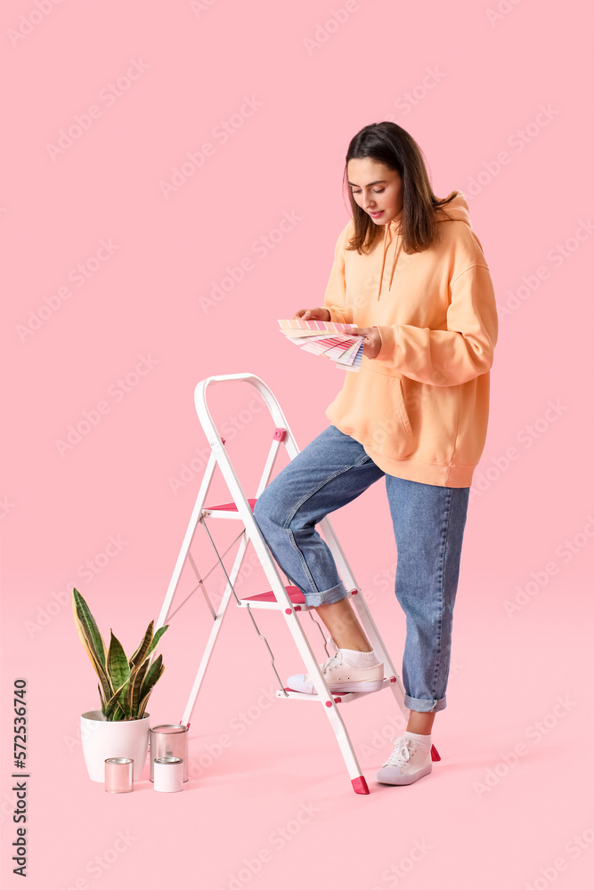 Young woman with paint palettes and ladder on pink background