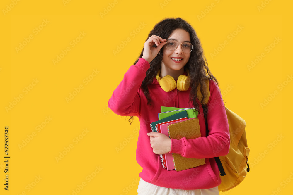 Female student with headphones, notebooks and backpack on yellow background