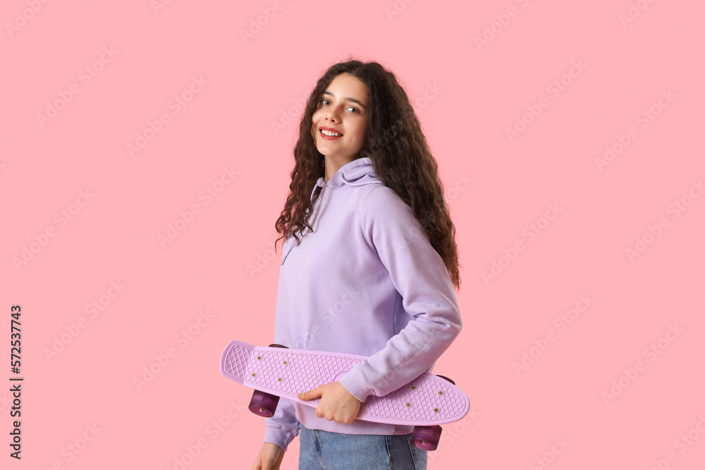 Teenage girl with skateboard on pink background