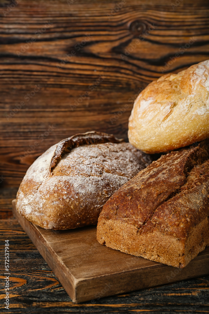 Cutting board with loaves of different fresh bread on wooden table