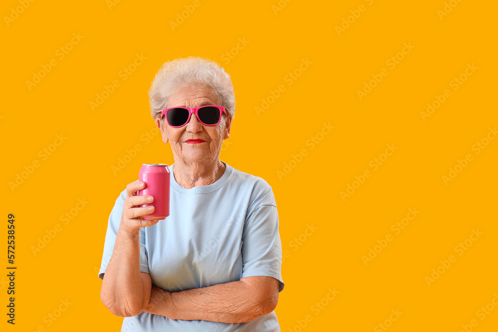 Senior woman in sunglasses with can of soda on yellow background