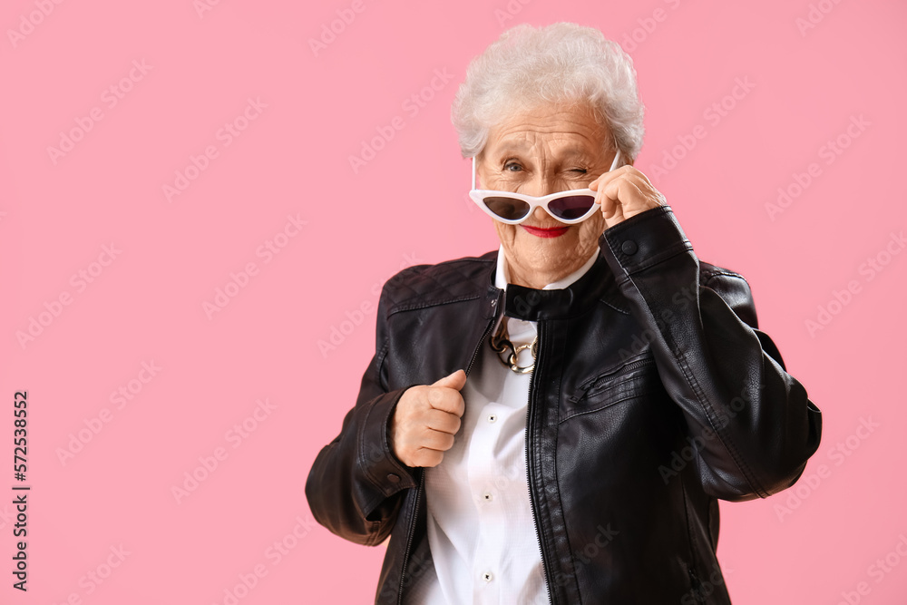 Senior woman in sunglasses winking on pink background