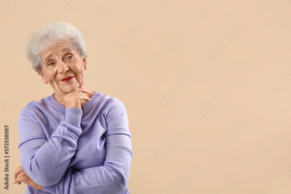 Thoughtful senior woman in lilac sweater on beige background