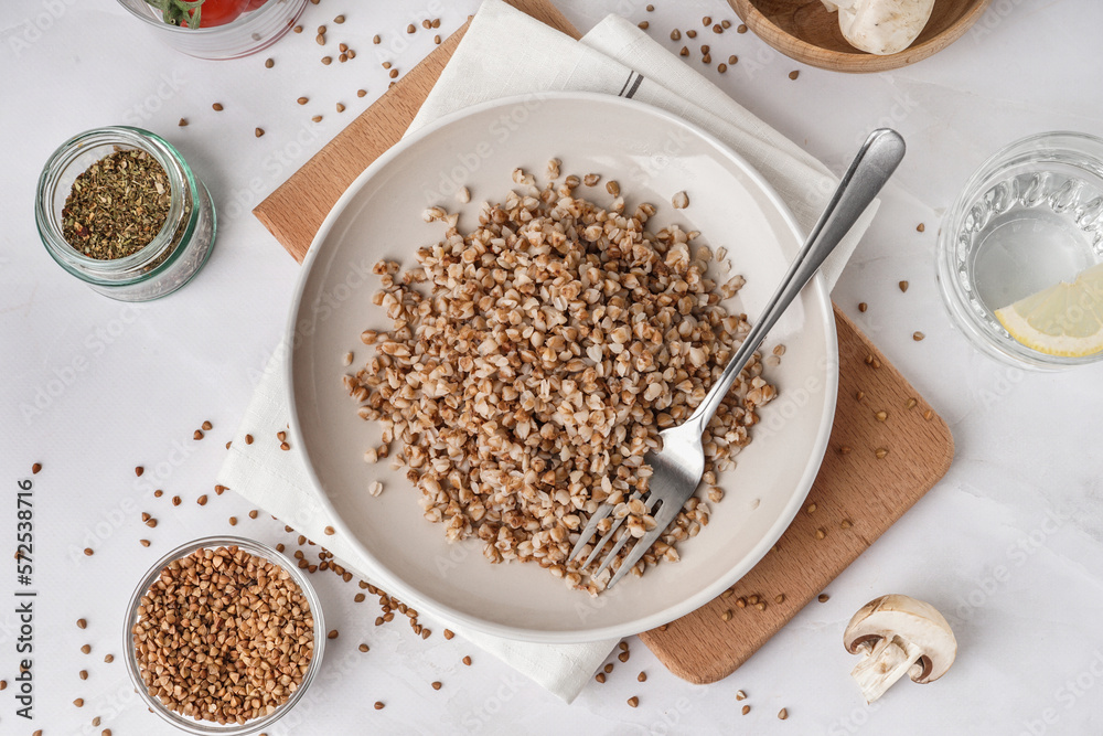 Board with plate of tasty buckwheat porridge on white table