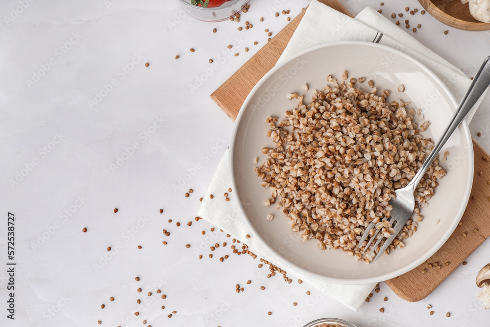 Board with plate of tasty buckwheat porridge on white table