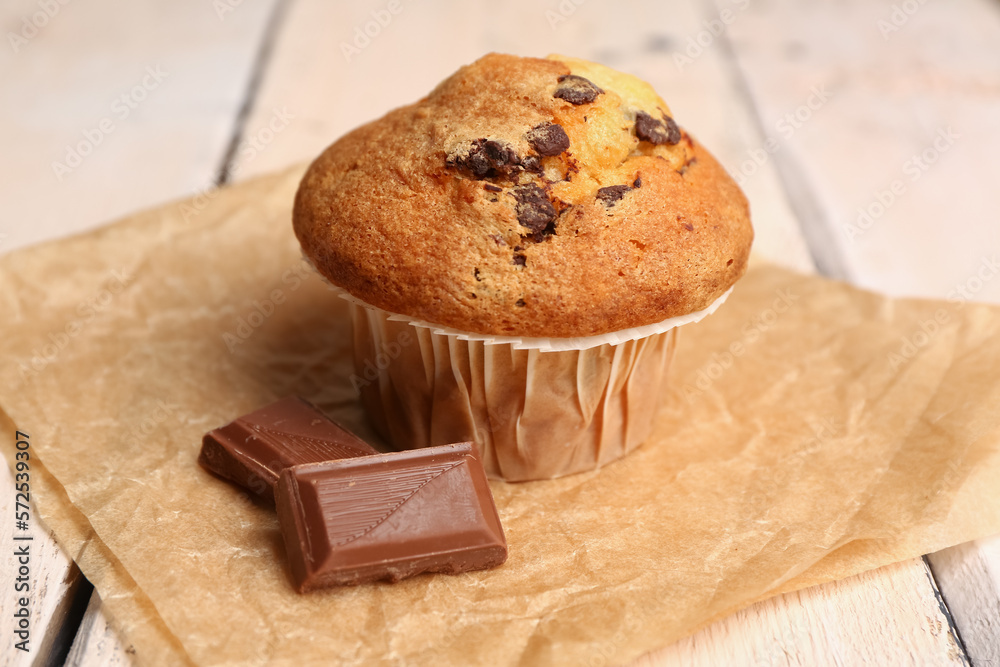 Tasty muffin and pieces of chocolate on light wooden table, closeup