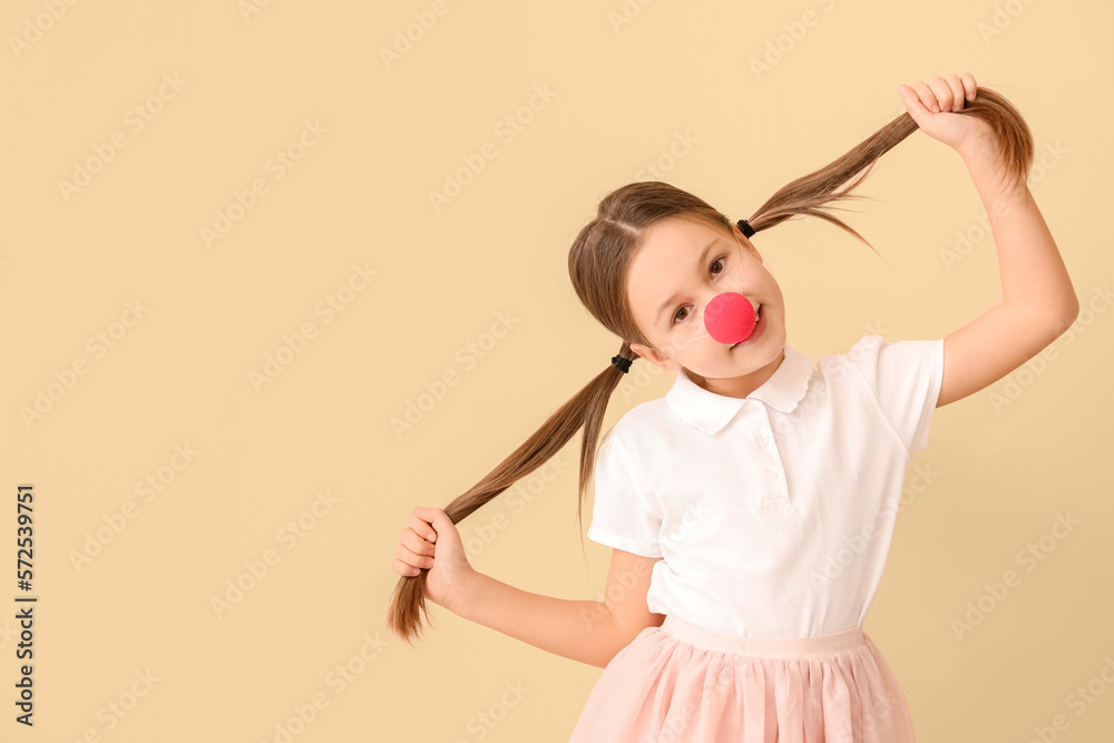 Little girl with clown nose on beige background. April Fools Day celebration