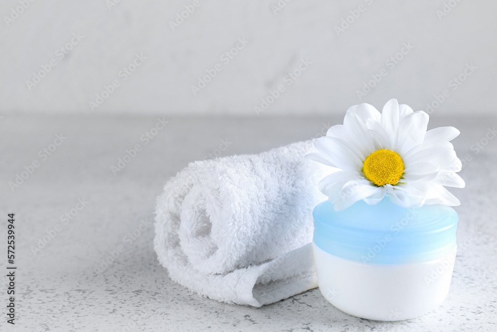 Jar of cosmetic product, towel and chamomile flower on light background