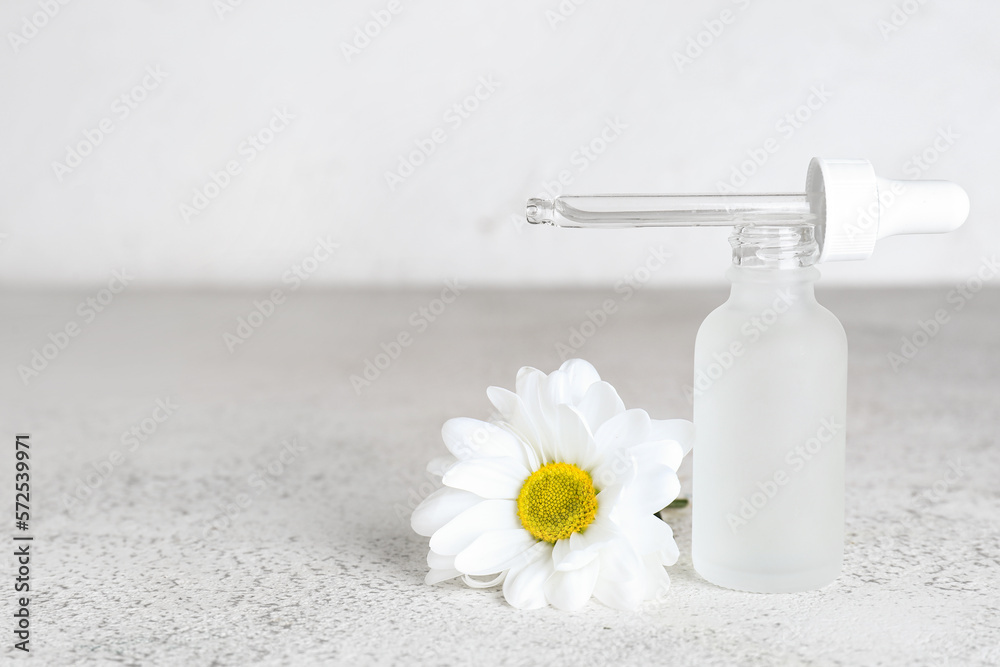 Bottle of essential oil and chamomile flower on light background