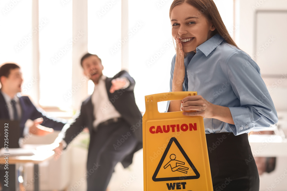 Young woman with caution sign playing a prank on her colleagues in office. April Fools Day celebrat