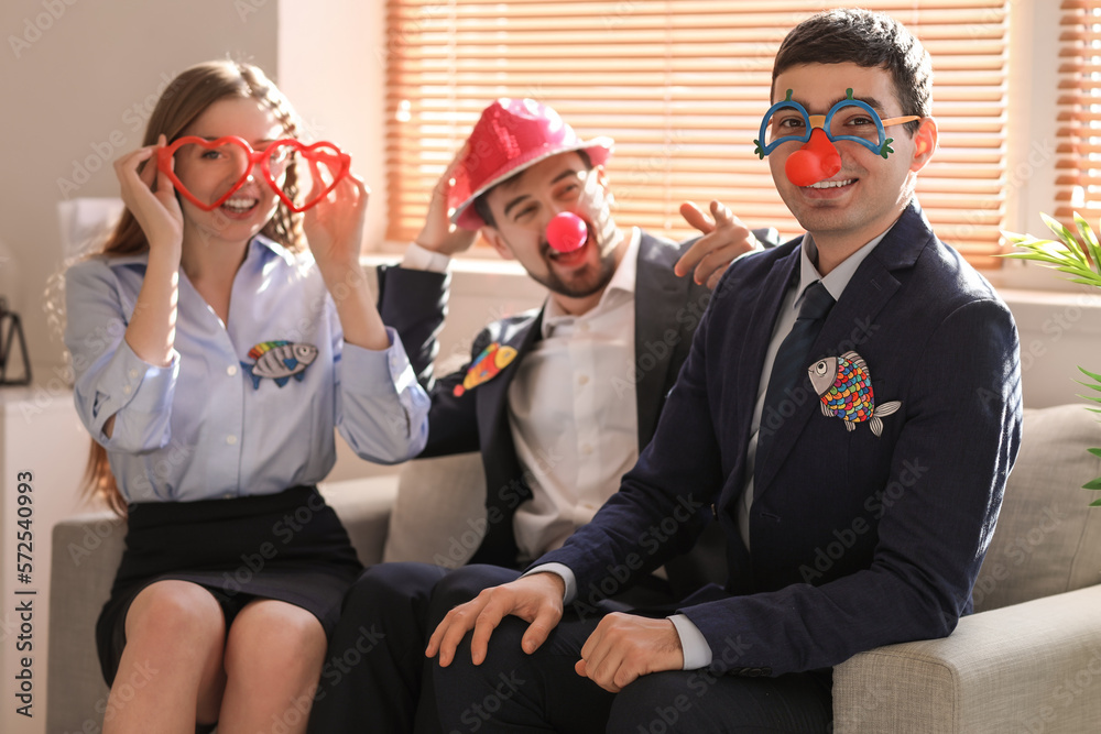 Colleagues with funny disguise sitting on sofa in office. April Fools Day celebration