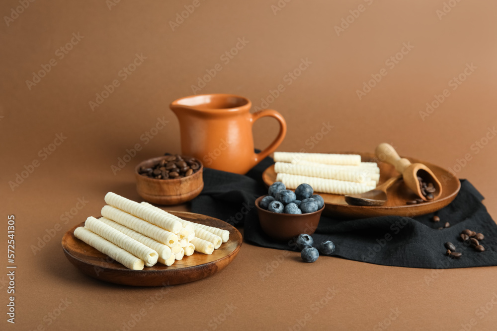 Plates with delicious wafer rolls, blueberries and coffee beans on brown background