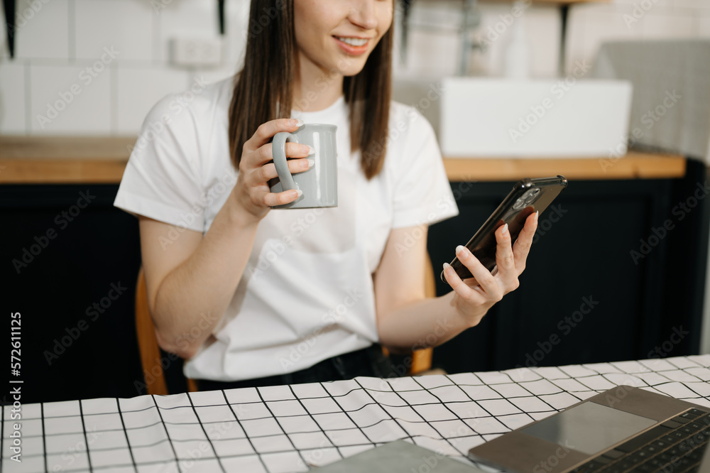 woman using laptop and typing on laptop and holding coffee cup in cafe, home office in morning light