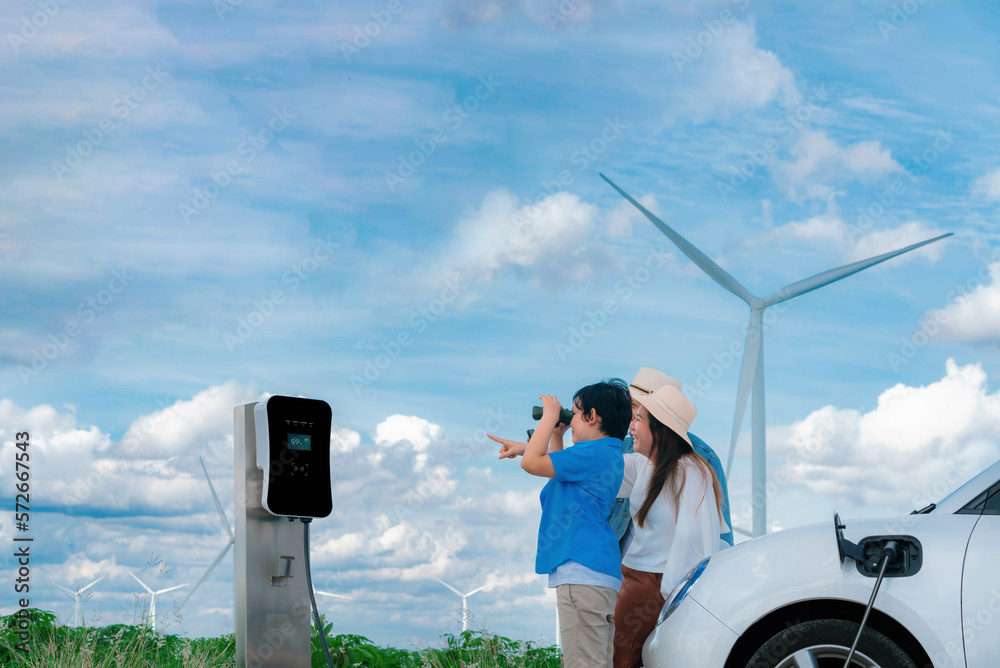 Concept of progressive happy family enjoying their time at wind farm with electric vehicle. Electric