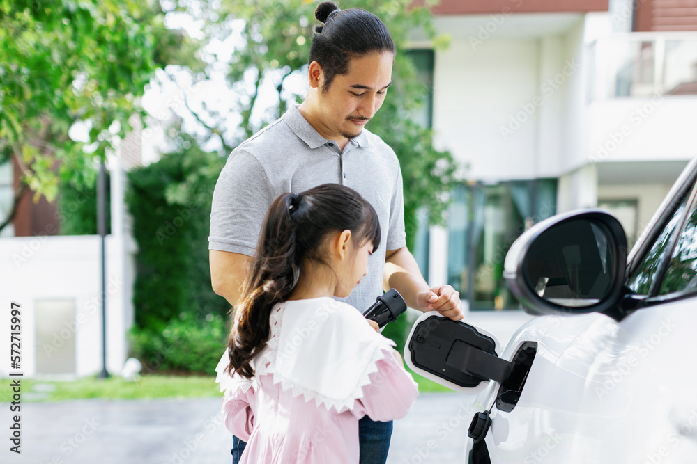 Progressive father and daughter returned from school in electric vehicle that is being charged at ho