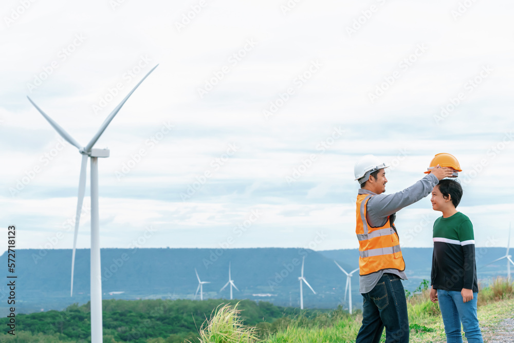 Engineer with his son on a wind farm atop a hill or mountain in the rural. Progressive ideal for the