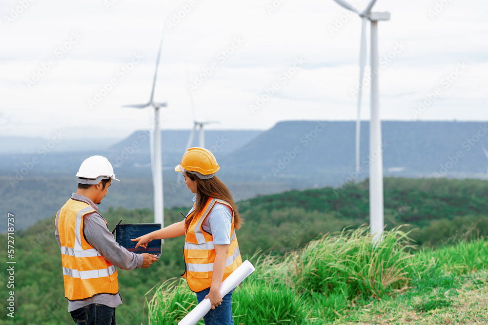 Male and female engineers working on a wind farm atop a hill or mountain in the rural. Progressive i