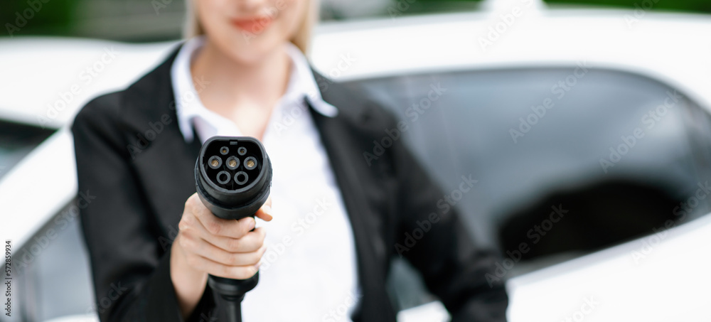 Blur closeup businesswoman hand holding and pointing an EV plug at camera for electric vehicle as pr