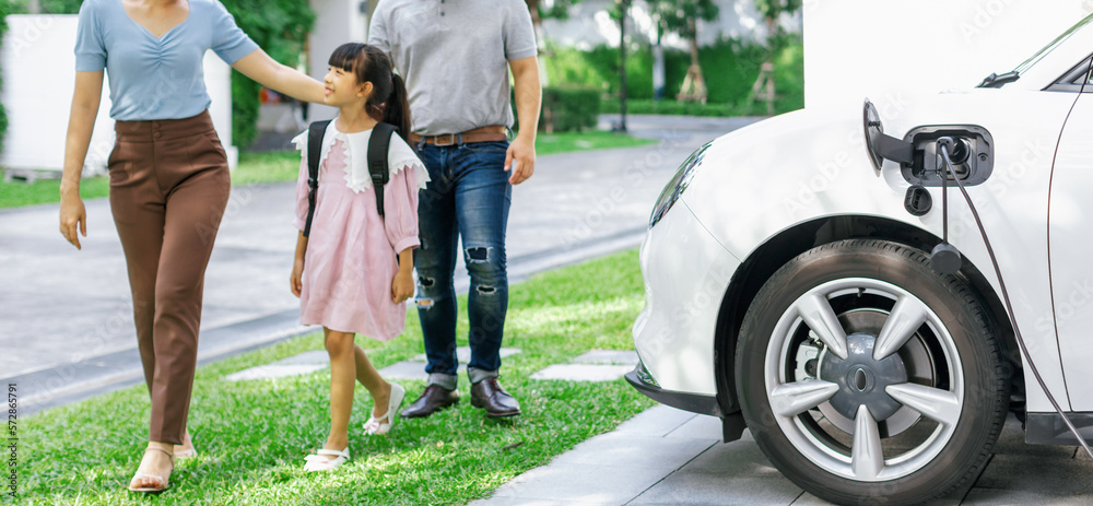 Progressive young happy family with electric vehicle and home backyard charging station. Green and c