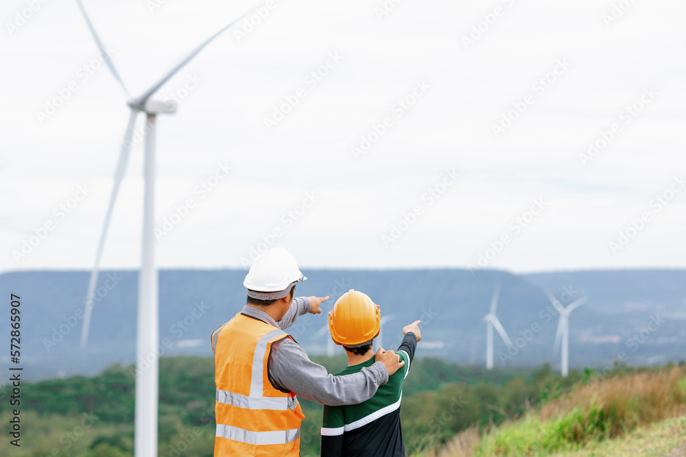 Engineer with his son on a wind farm atop a hill or mountain in the rural. Progressive ideal for the