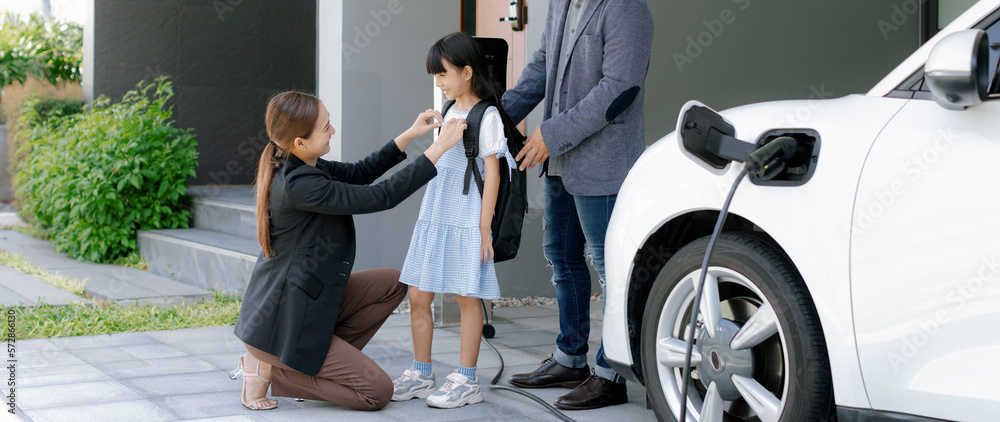 Progressive young parents and daughter with electric vehicle and home charging station. Green and cl