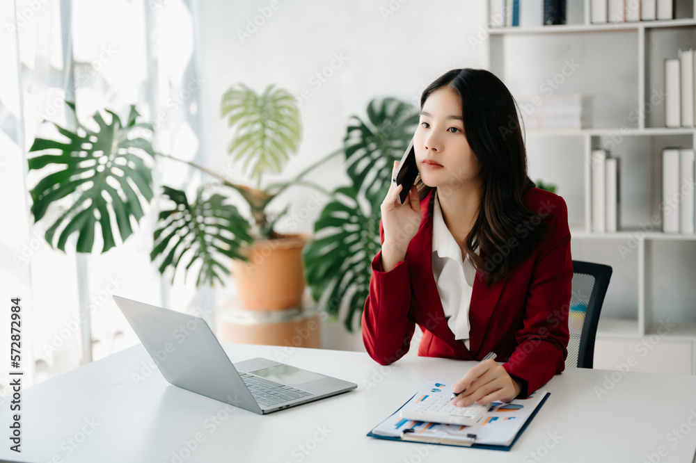 Business asian woman Talking on the phone and using a laptop with a smile while sitting at office