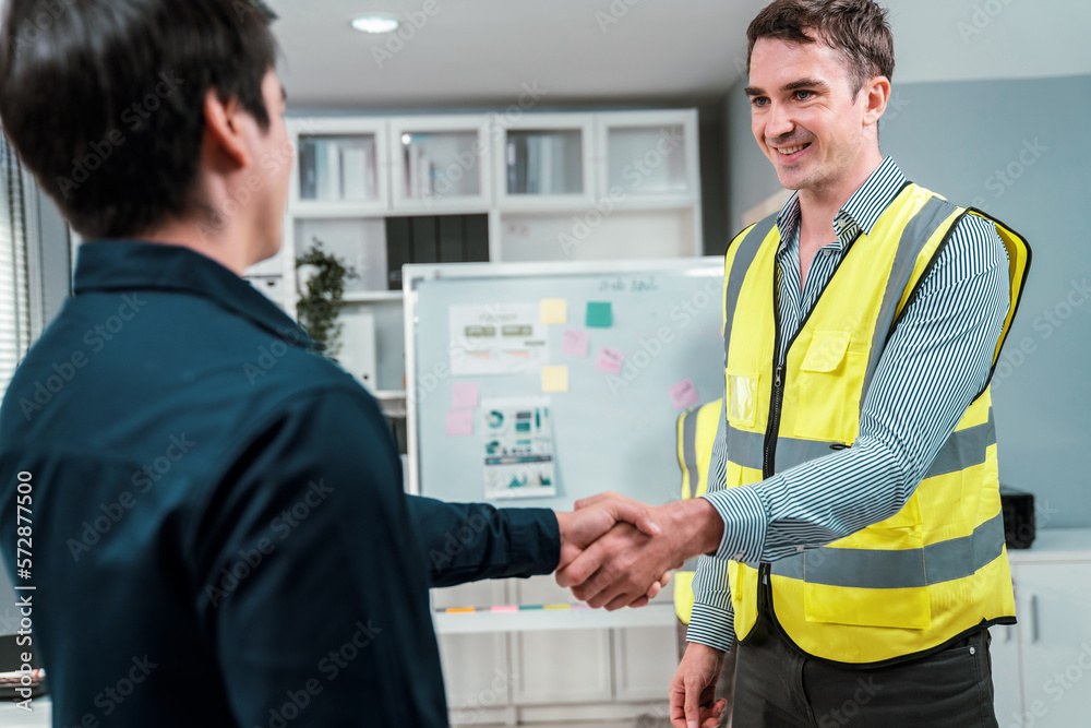 An engineer with a protective vest handshake with an investor in his office. Following a successful 