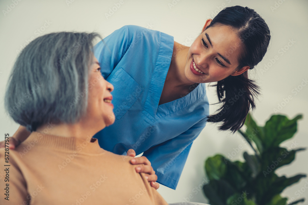 A caregiver rest her hands on the shoulders of a contented senior patient while she sitting on the s