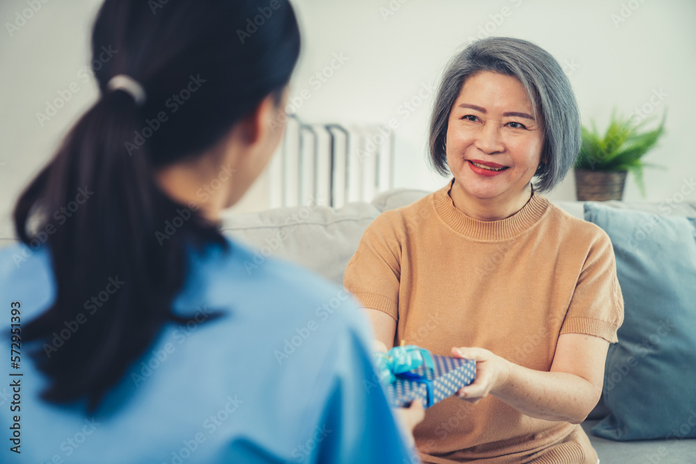 A young caregiver hand over to her senior patient a blue gift box with blue ribbons at a contented l