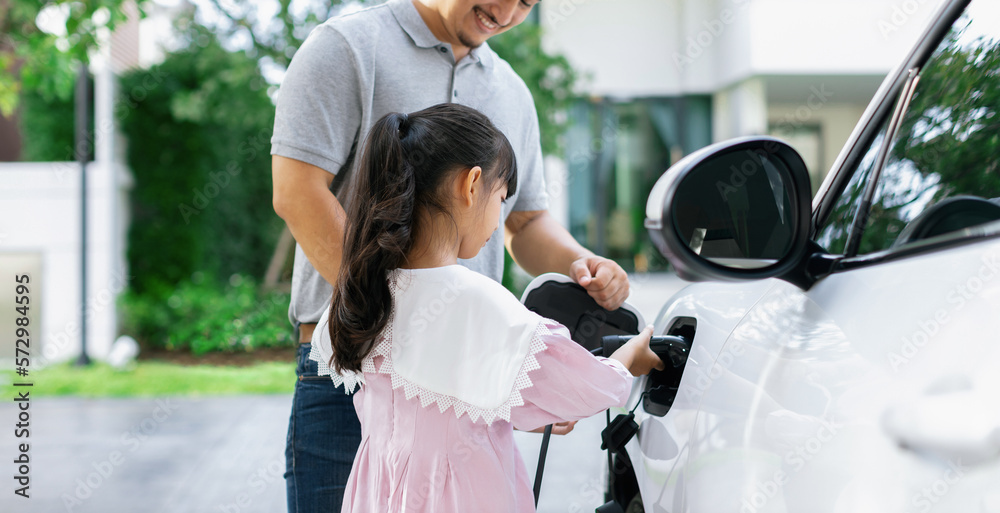 Progressive father and daughter returned from school in electric vehicle that is being charged at ho