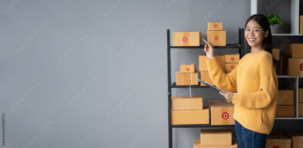 Happy young online business shop owner writing down the e-commerce details on the board while prepar