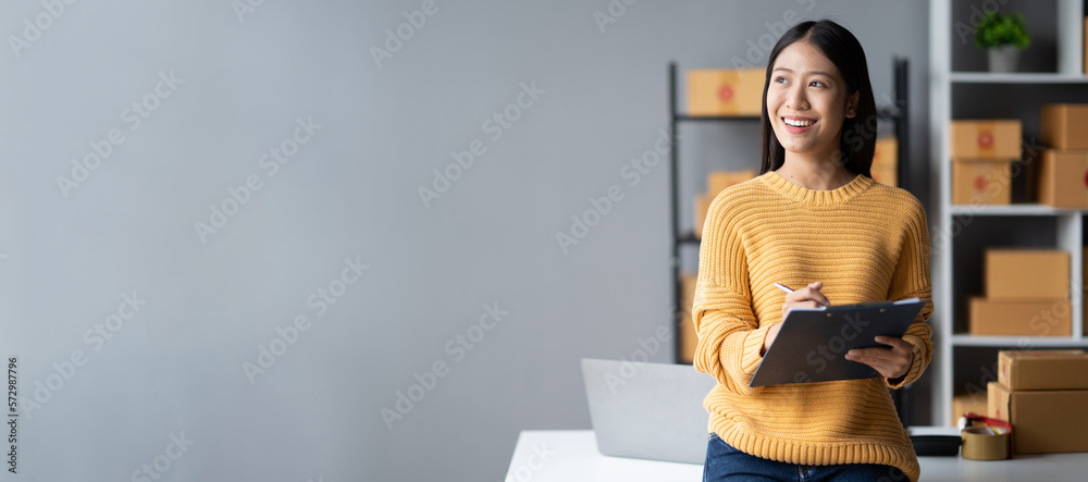 Happy young online business shop owner writing down the e-commerce details on the board while prepar