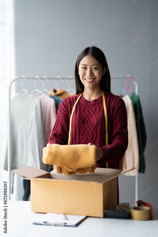 Young Asian shop owner packing her product for customer, putting cloth down in the box, ready to sen