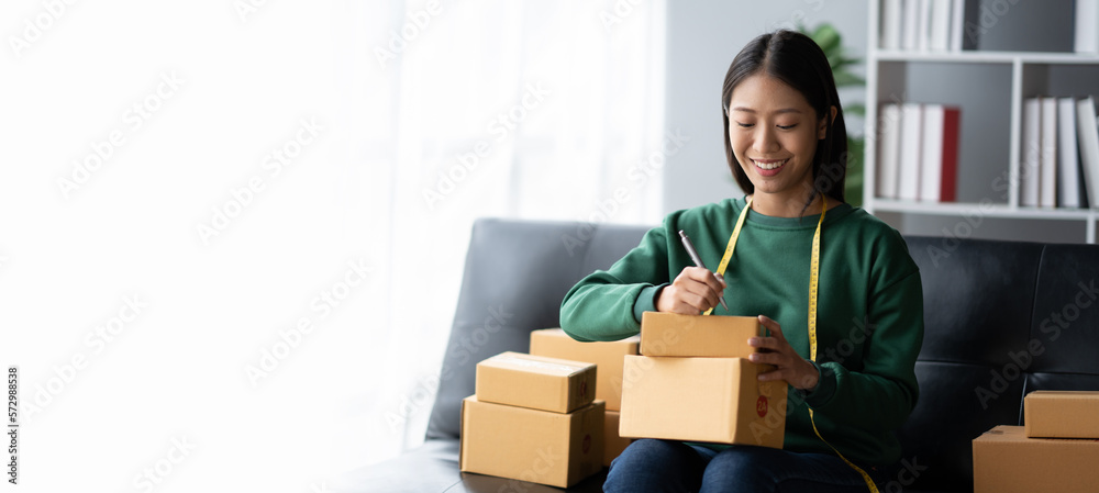 Lovely Asian business owner writing down the details of the customers on the parcel boxes before dis