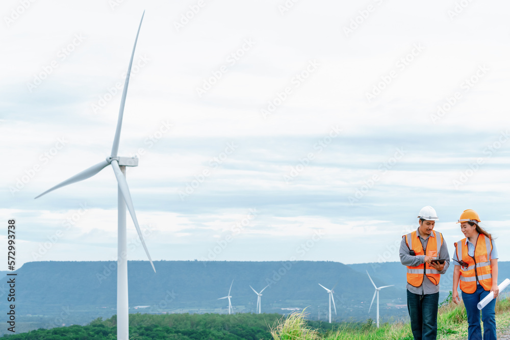 Male and female engineers working on a wind farm atop a hill or mountain in the rural. Progressive i