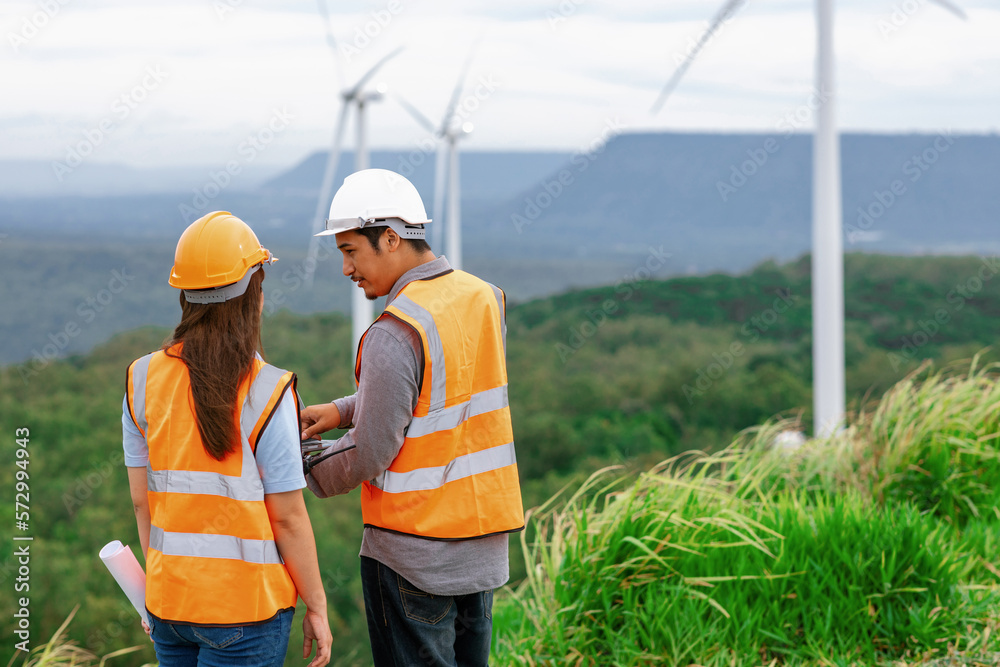 Male and female engineers working on a wind farm atop a hill or mountain in the rural. Progressive i