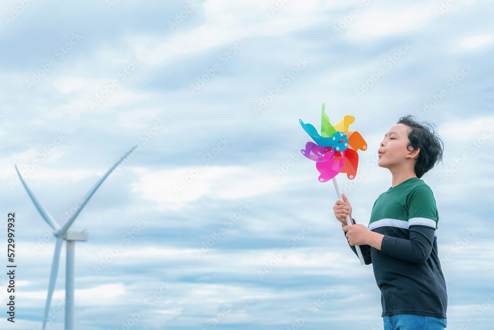 Progressive young asian boy playing with wind pinwheel toy in the wind turbine farm, green field ove