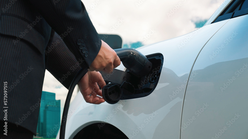 Progressive businessman recharge his electric vehicle with charger cable plug from charging station 