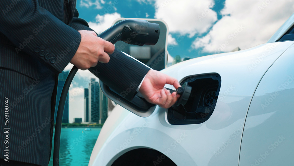 Progressive businessman recharge his electric vehicle with charger cable plug from charging station 