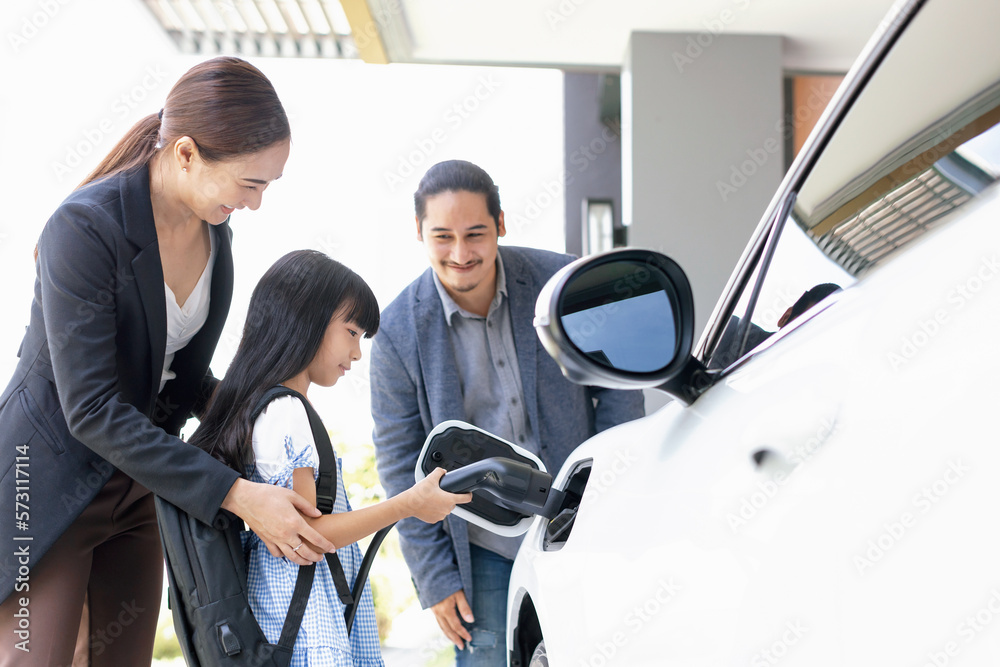 Progressive young parents and daughter with electric vehicle and home charging station. Green and cl