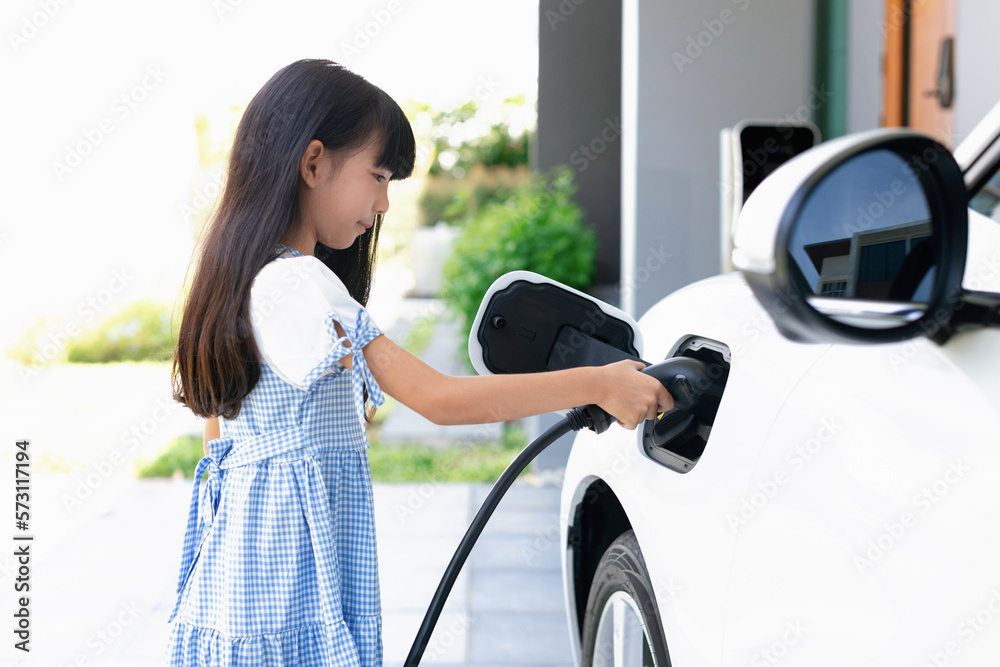 A playful girl holding an EV plug, a home charging station providing a sustainable power source for 